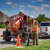 Construction worker operating vacuum truck with safety cones near residential area