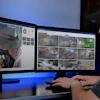 Security professional monitoring multiple surveillance camera feeds on dual computer screens