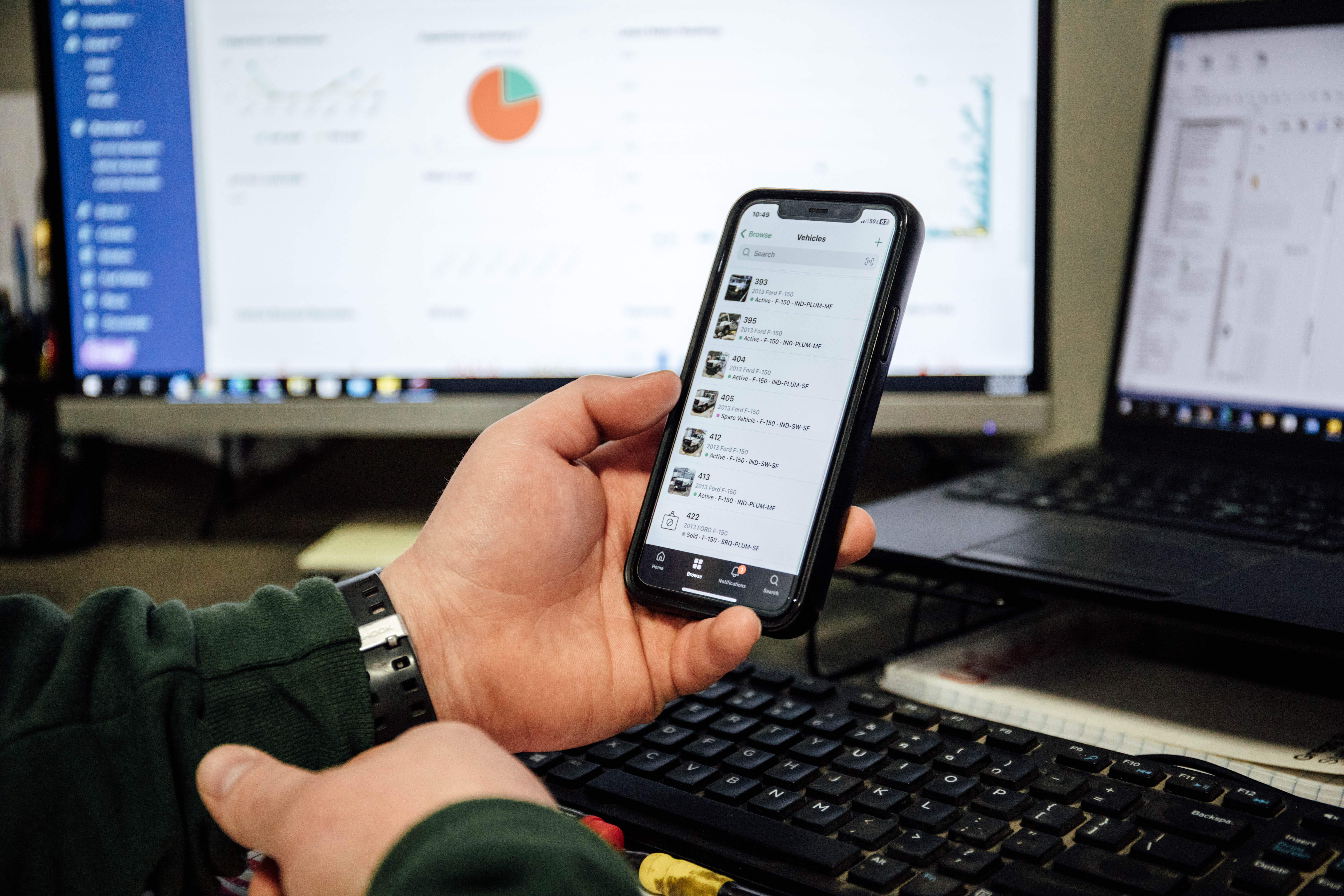 Hand holding smartphone with messaging app, laptop and data chart in background