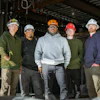 Construction team in hard hats and safety glasses standing in industrial workspace