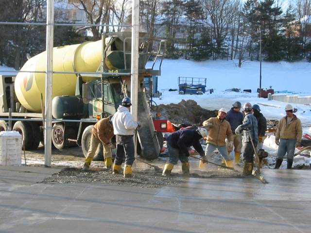 Construction workers pouring concrete beside a yellow cement mixer in winter