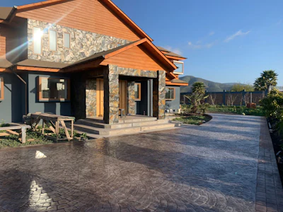Modern stone and wood house with stamped concrete driveway, mountain landscape background