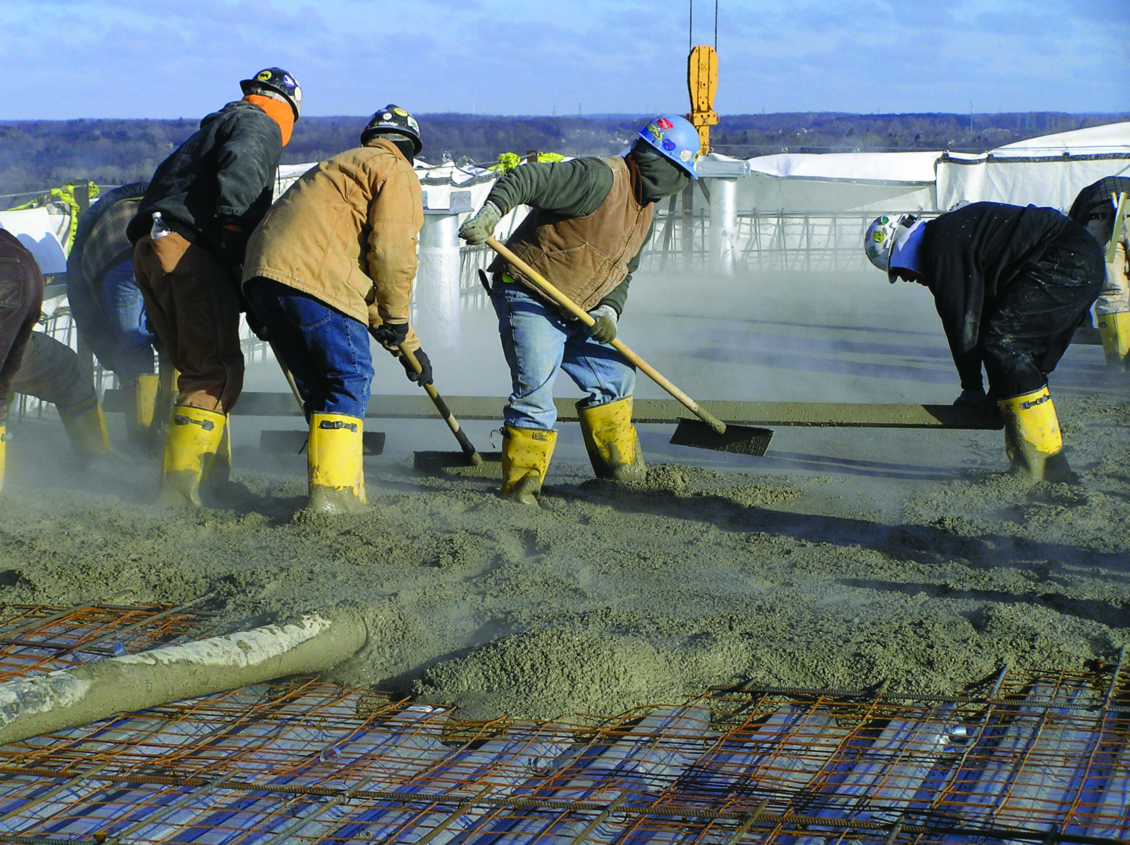 Construction workers spreading concrete on rebar mesh at industrial site