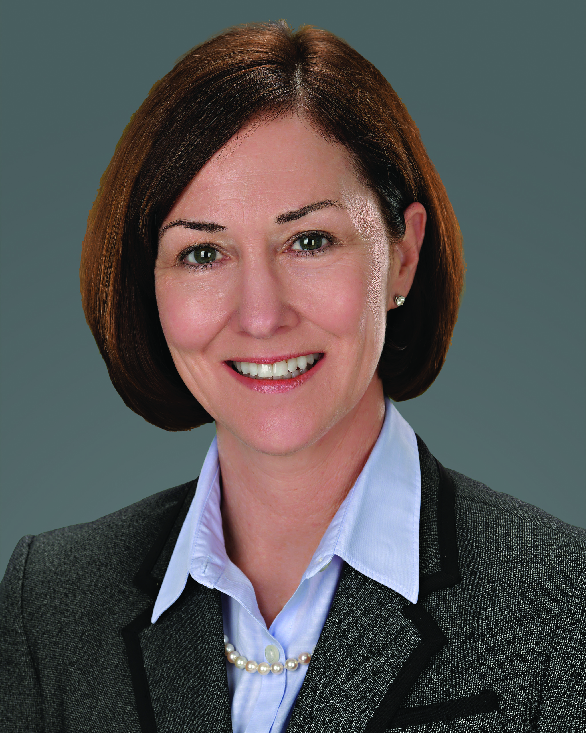Professional woman in gray blazer smiling with pearl necklace