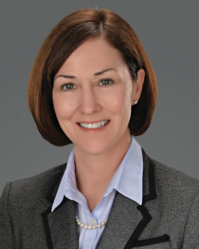 Professional woman in gray blazer smiling with pearl necklace