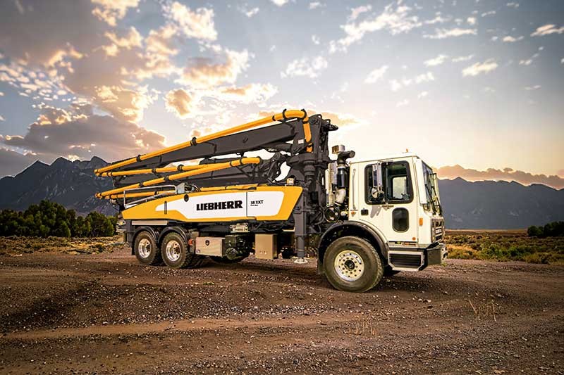 Liebherr concrete pump truck parked on dirt ground with mountain landscape at sunset
