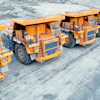 Large orange and blue mining haul trucks lined up on rocky terrain