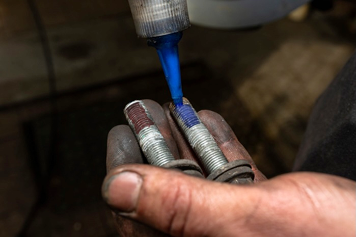 Hand applying blue threadlocker liquid to metal bolts