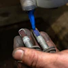 Hand applying blue threadlocker liquid to metal bolts