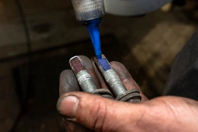 Hand applying blue threadlocker liquid to metal bolts