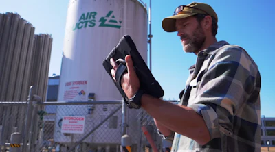 Worker checking equipment near Air CTS industrial storage tank with safety signage