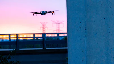 Drone hovering near concrete wall with power lines at twilight