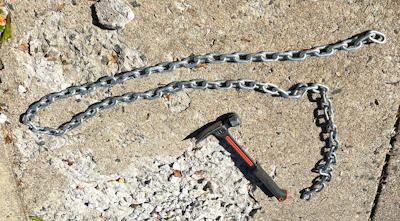 Metal chain links and a black hammer with red accent on rocky ground