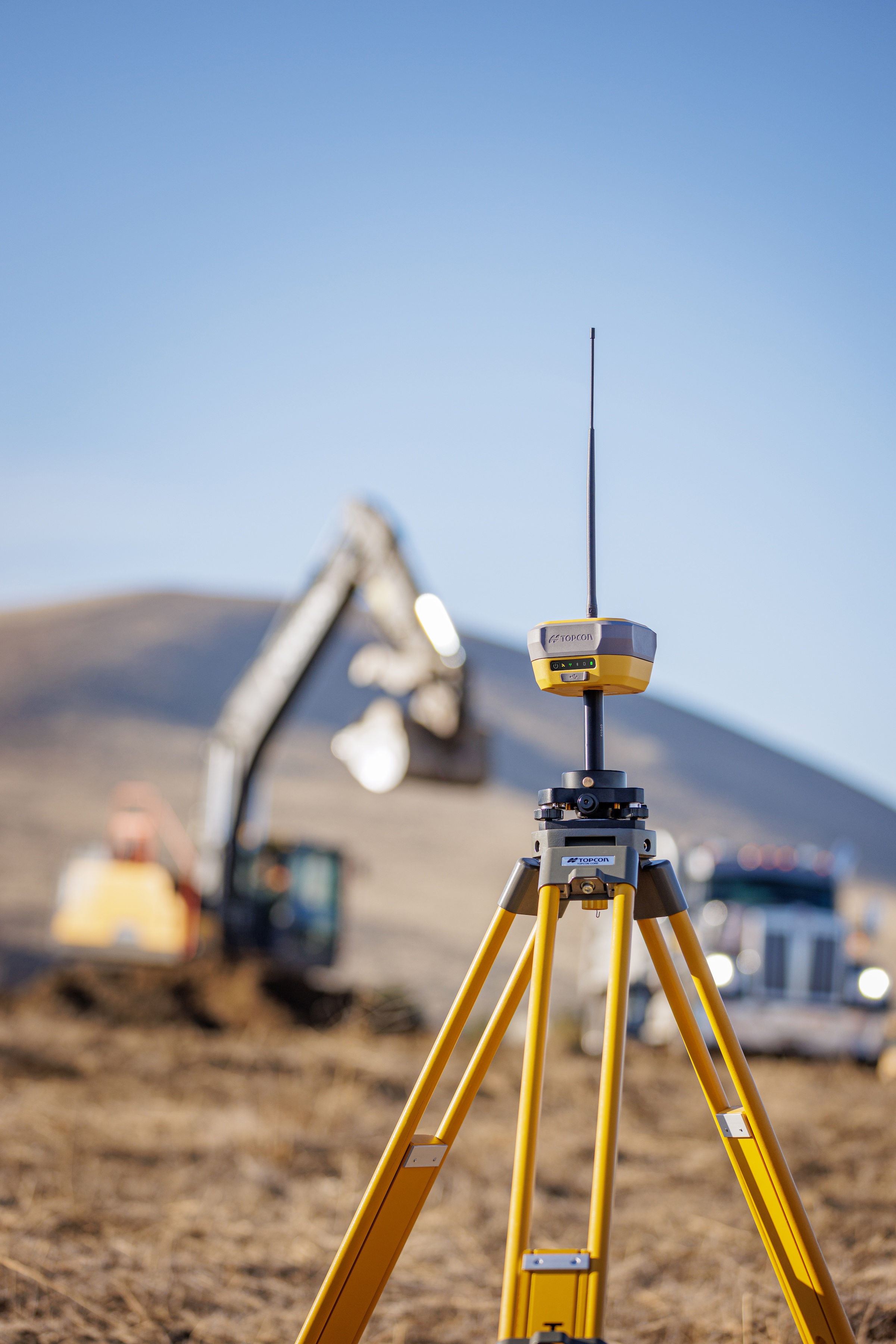 Yellow surveying GPS equipment on tripod at construction site with excavator