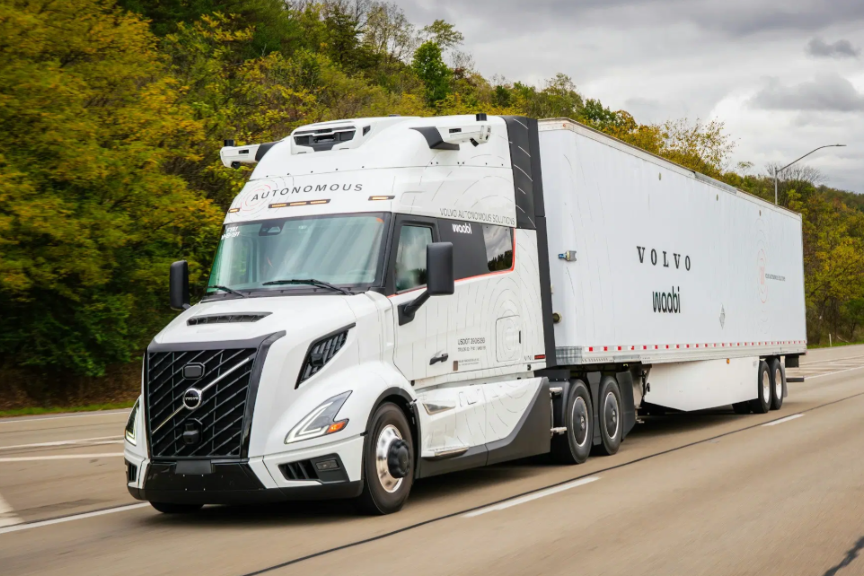 White Volvo autonomous semi-truck driving on highway with trees in background
