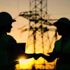 Two construction workers shaking hands at sunset near electrical towers