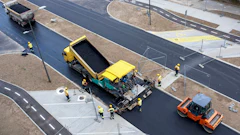 Road construction site with yellow paver, orange roller, and workers laying fresh asphalt