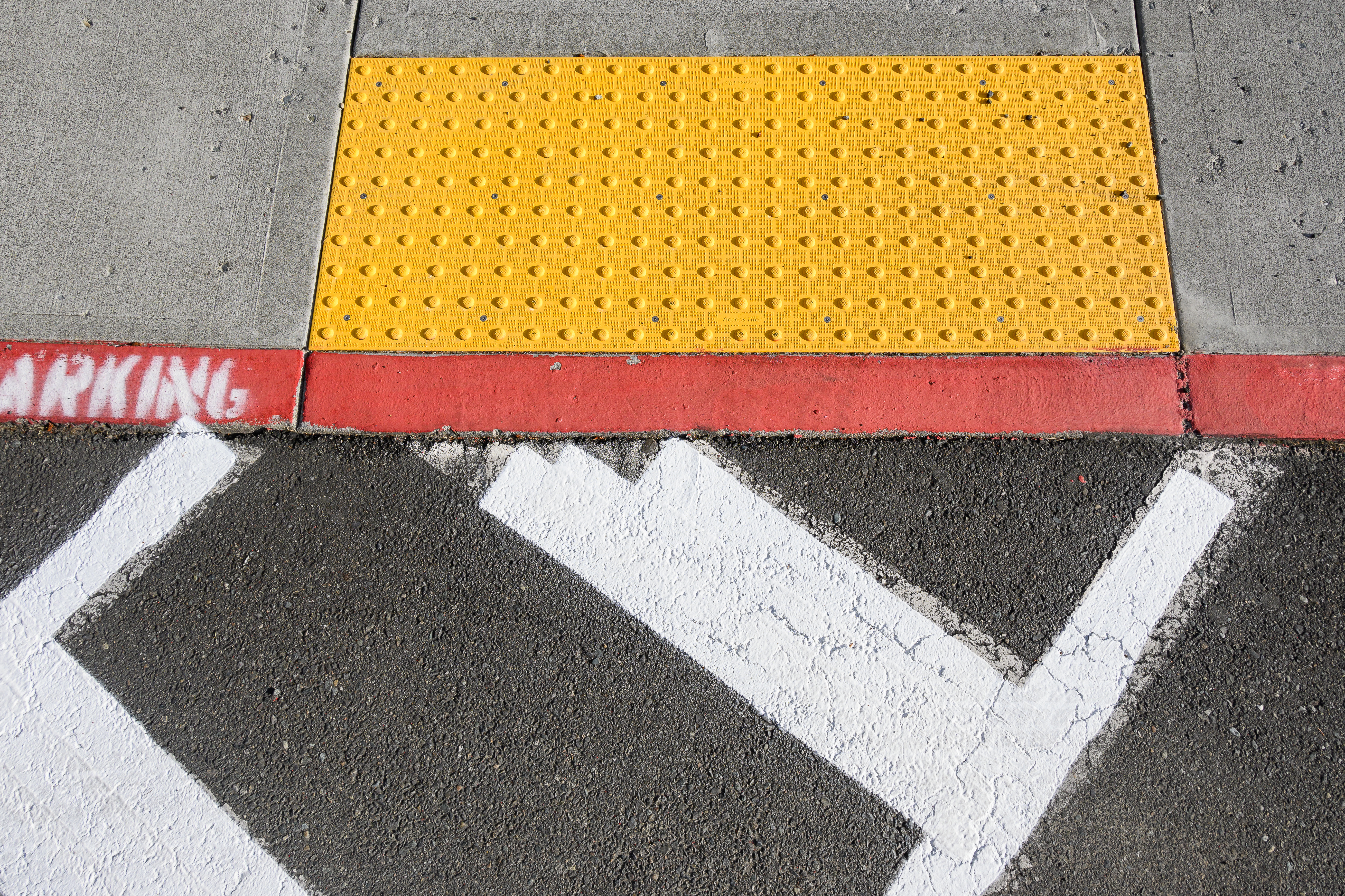 Yellow tactile warning surface on concrete sidewalk with white crosswalk markings