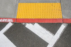 Yellow tactile warning surface on concrete sidewalk with white crosswalk markings