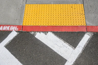 Yellow tactile warning surface on concrete sidewalk with white crosswalk markings