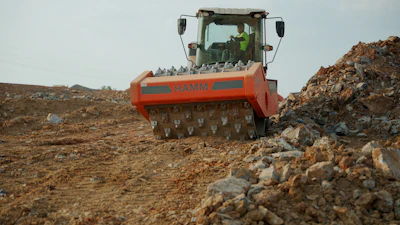 Orange Hamm compactor working on rocky construction site with debris piles
