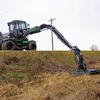 Green and black forestry harvester machine extending long mechanical arm across grassy field