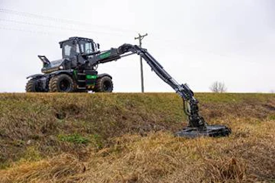 Green and black forestry harvester machine extending long mechanical arm across grassy field