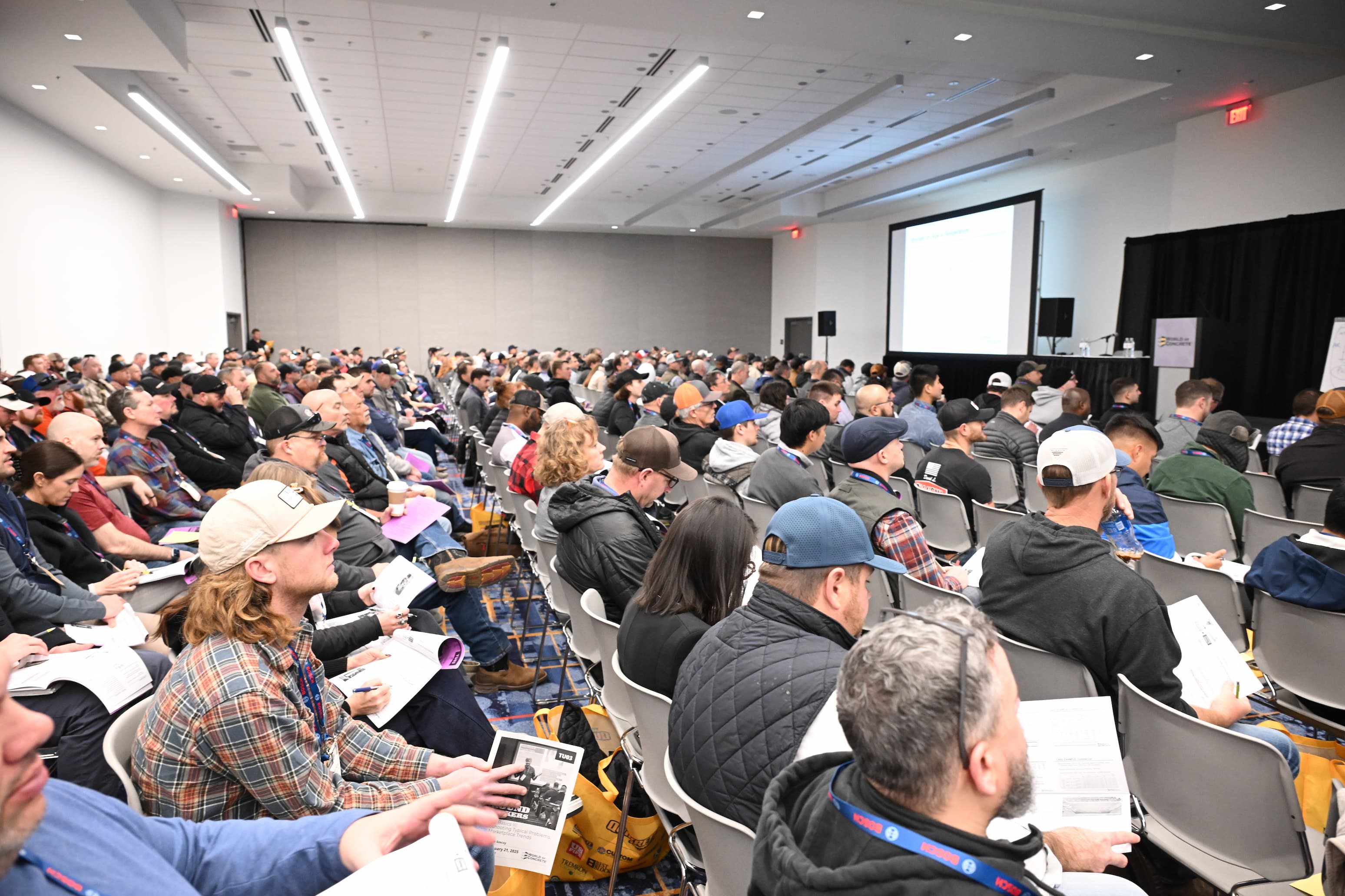 Crowded conference room with attendees seated, facing a presentation screen