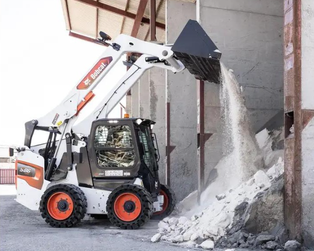 Bobcat skid-steer loader dumping concrete debris inside an industrial building