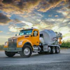 Yellow Kenworth concrete mixer truck parked on asphalt with dramatic sunset sky