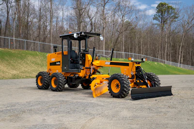 Bright orange motor grader on gravel lot with trees and grass in background