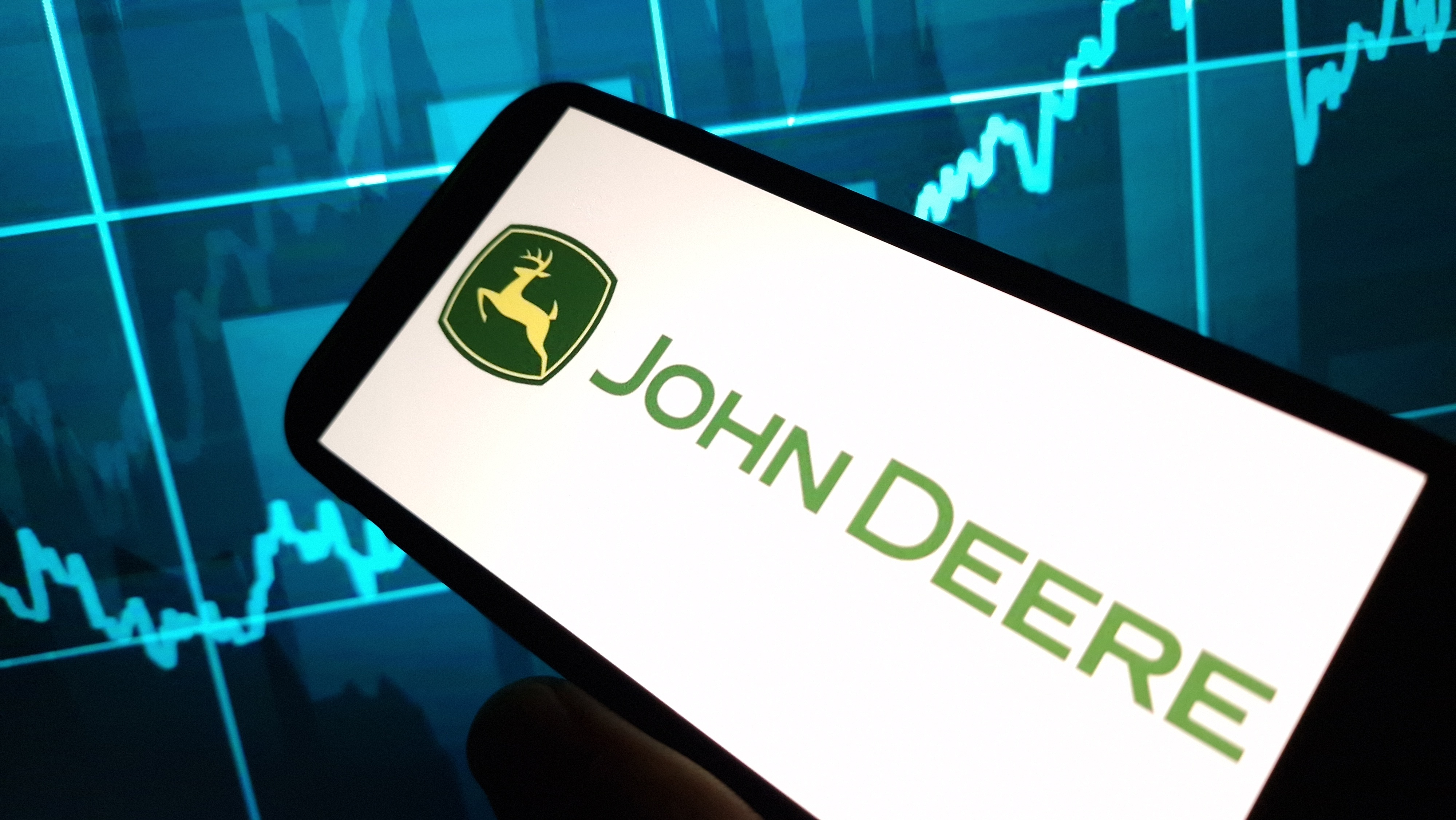 John Deere logo on smartphone screen with financial market graph backdrop