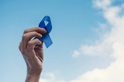 Blue awareness ribbon raised against cloudy blue sky
