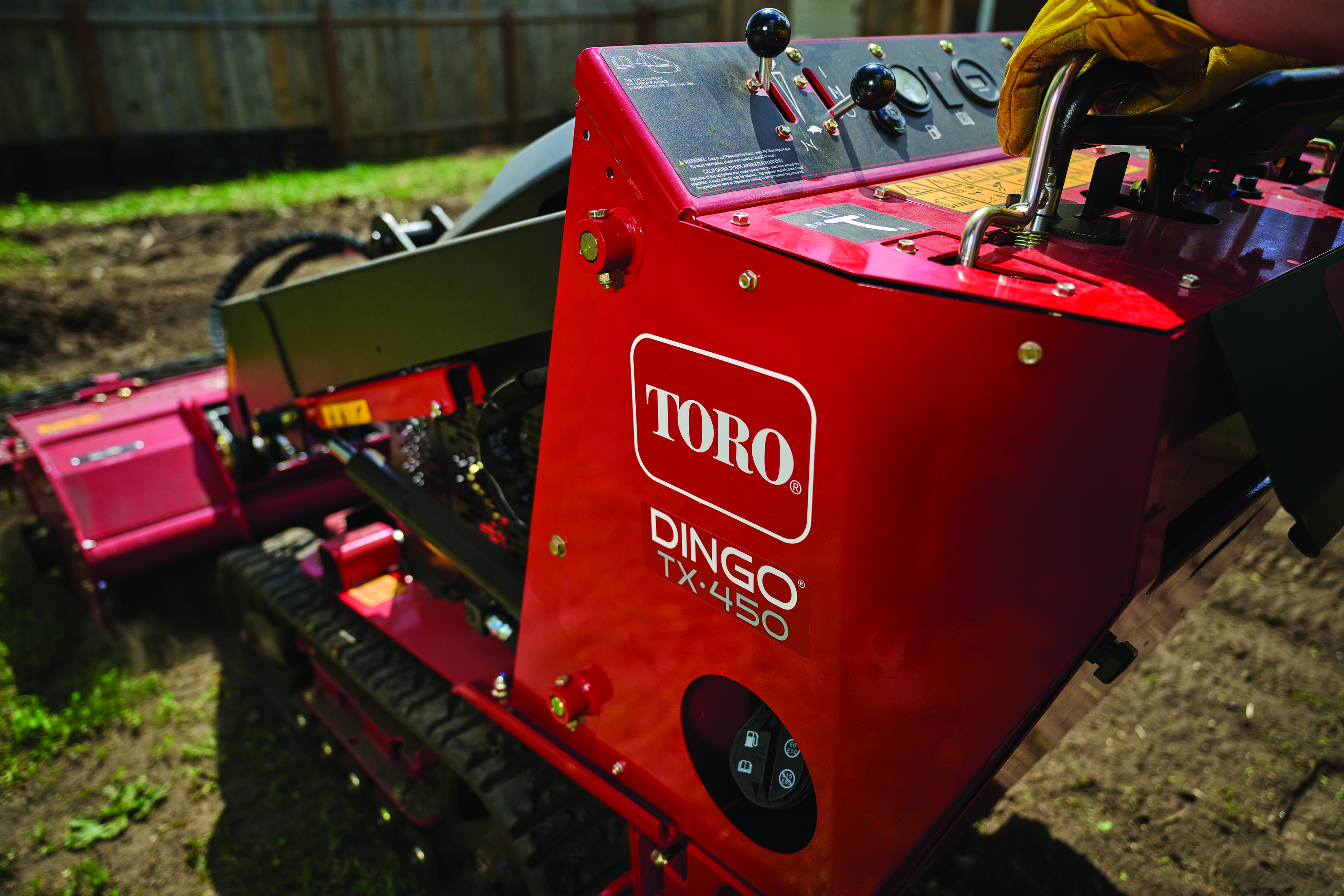 Red Toro Dingo TX-480 tracked utility machine on dirt ground near wooden fence