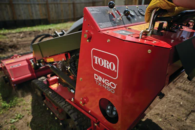 Red Toro Dingo TX-480 tracked utility machine on dirt ground near wooden fence