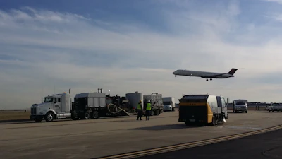 Airport tarmac with ground service vehicles and commercial airplane taking off