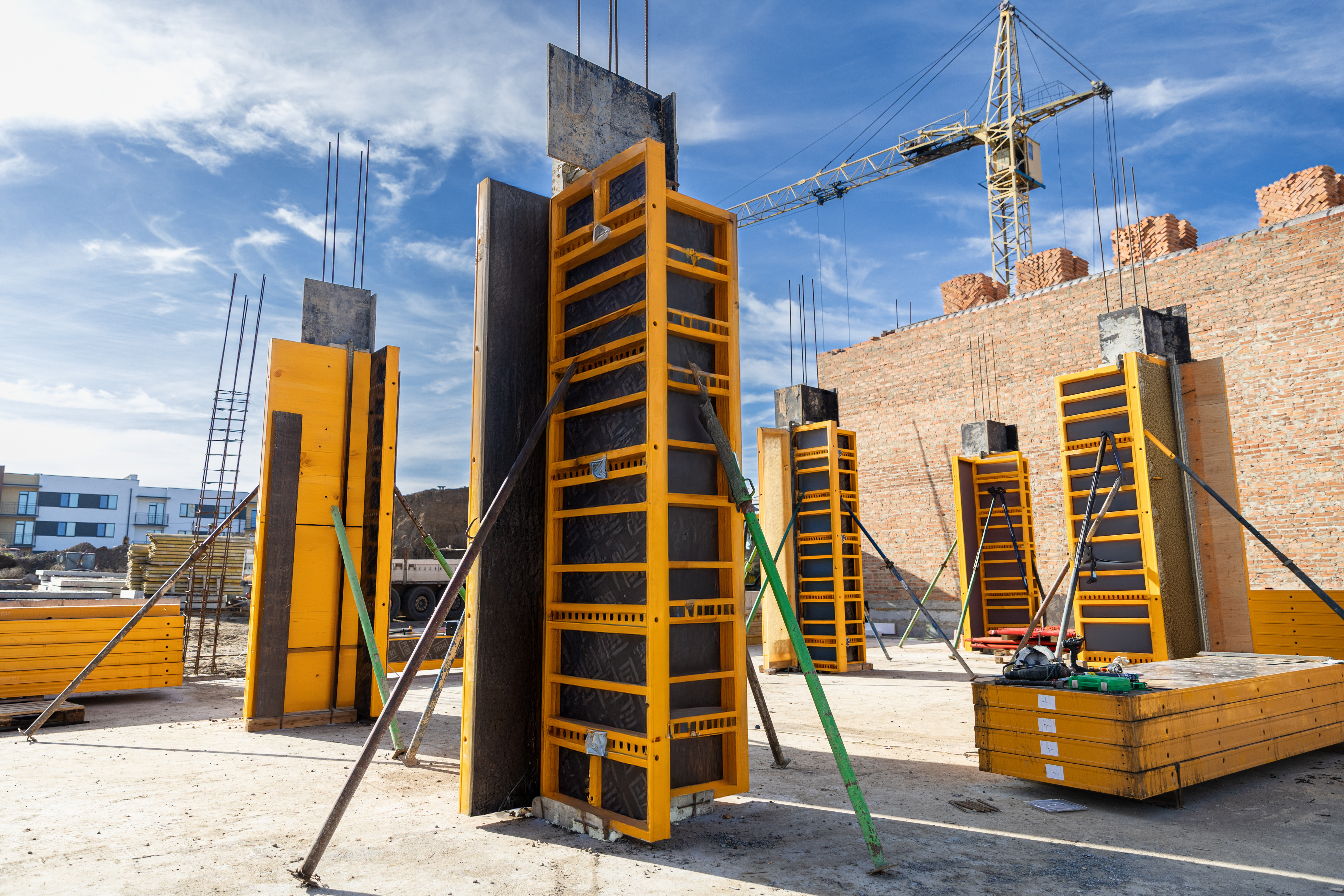 Yellow construction formwork panels and crane at building site with brick walls