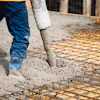 Construction worker pouring concrete over steel reinforcement mesh