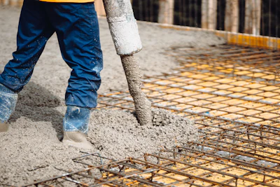Construction worker pouring concrete over steel reinforcement mesh