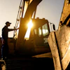 Construction worker climbing excavator at sunrise with golden backlighting