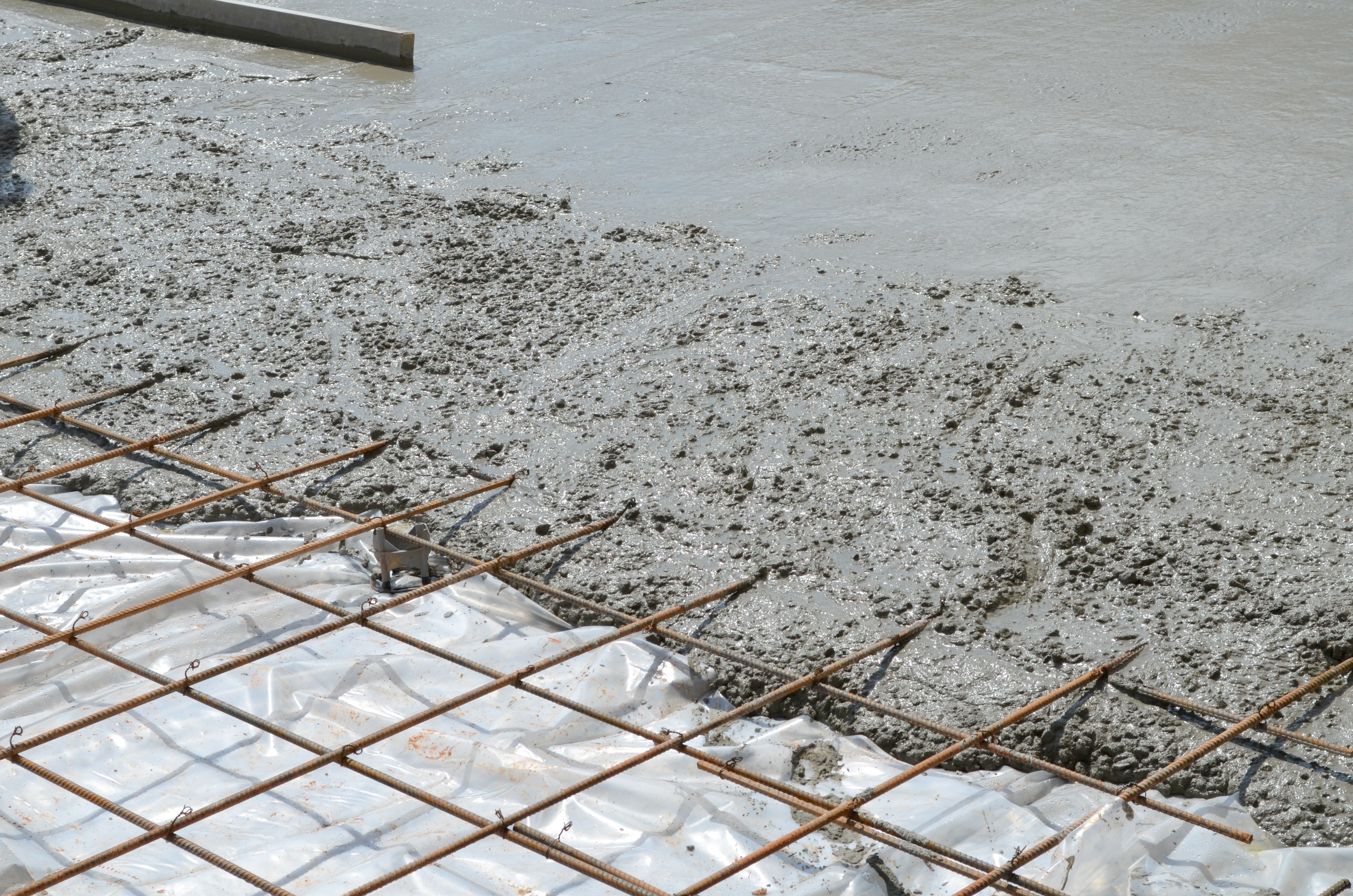 Wet concrete being poured over steel reinforcement grid during construction