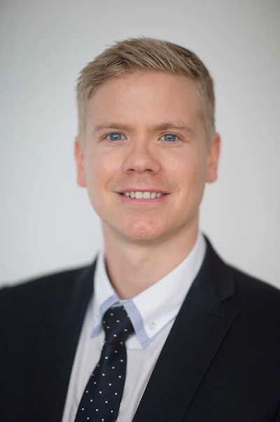 Professional smiling man in black suit and polka dot tie against neutral background