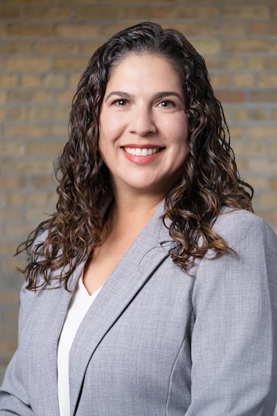 Professional woman in gray blazer smiling against brick wall backdrop