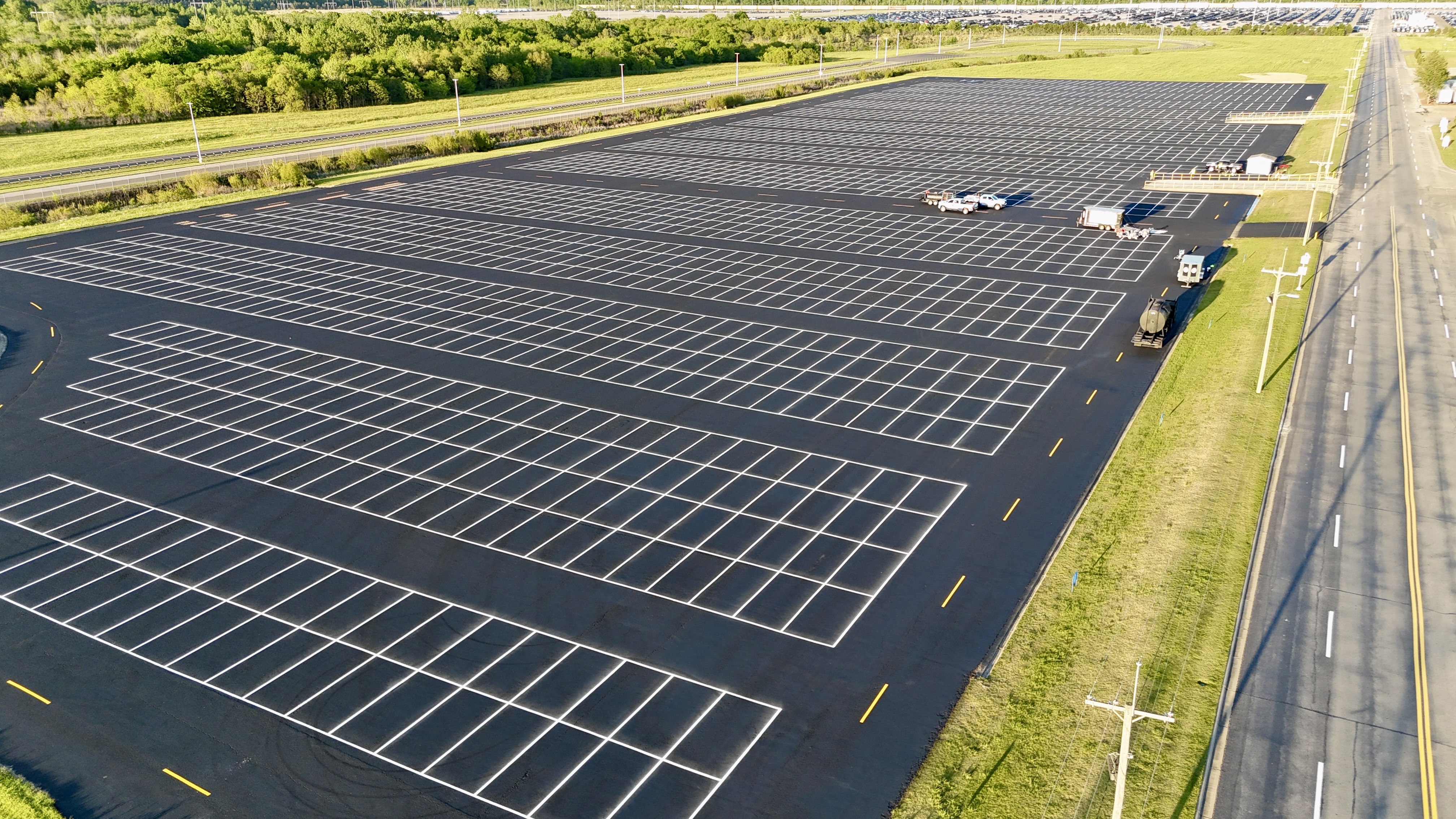 Aerial view of empty parking lot with white lines, next to highway and green landscape
