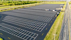 Aerial view of empty parking lot with white lines, next to highway and green landscape