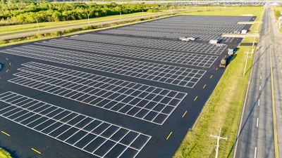 Aerial view of empty parking lot with white lines, next to highway and green landscape