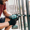 Worker drilling metal fence wearing black gloves and red shirt