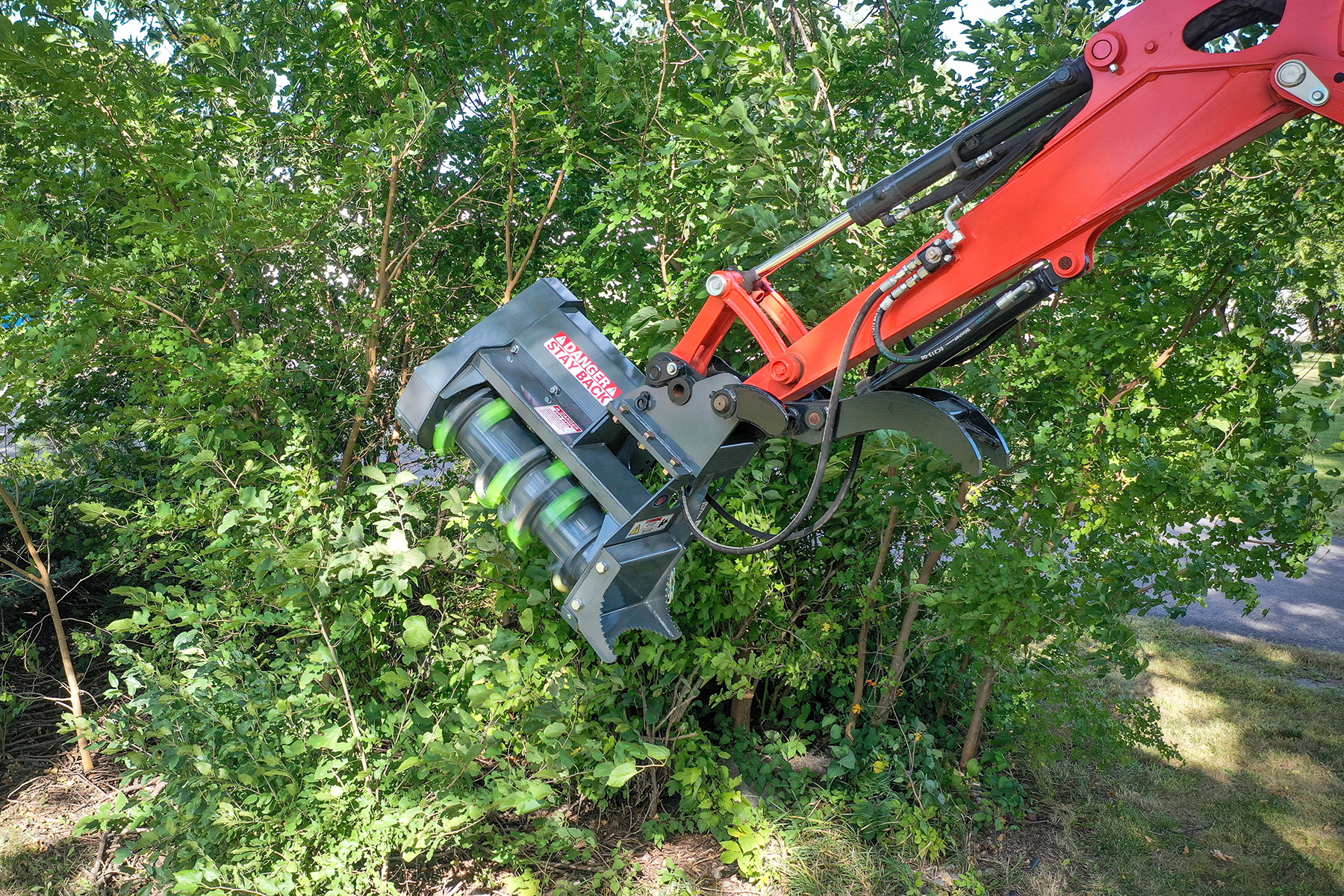 Red and gray mechanical excavator attachment clearing vegetation among green trees