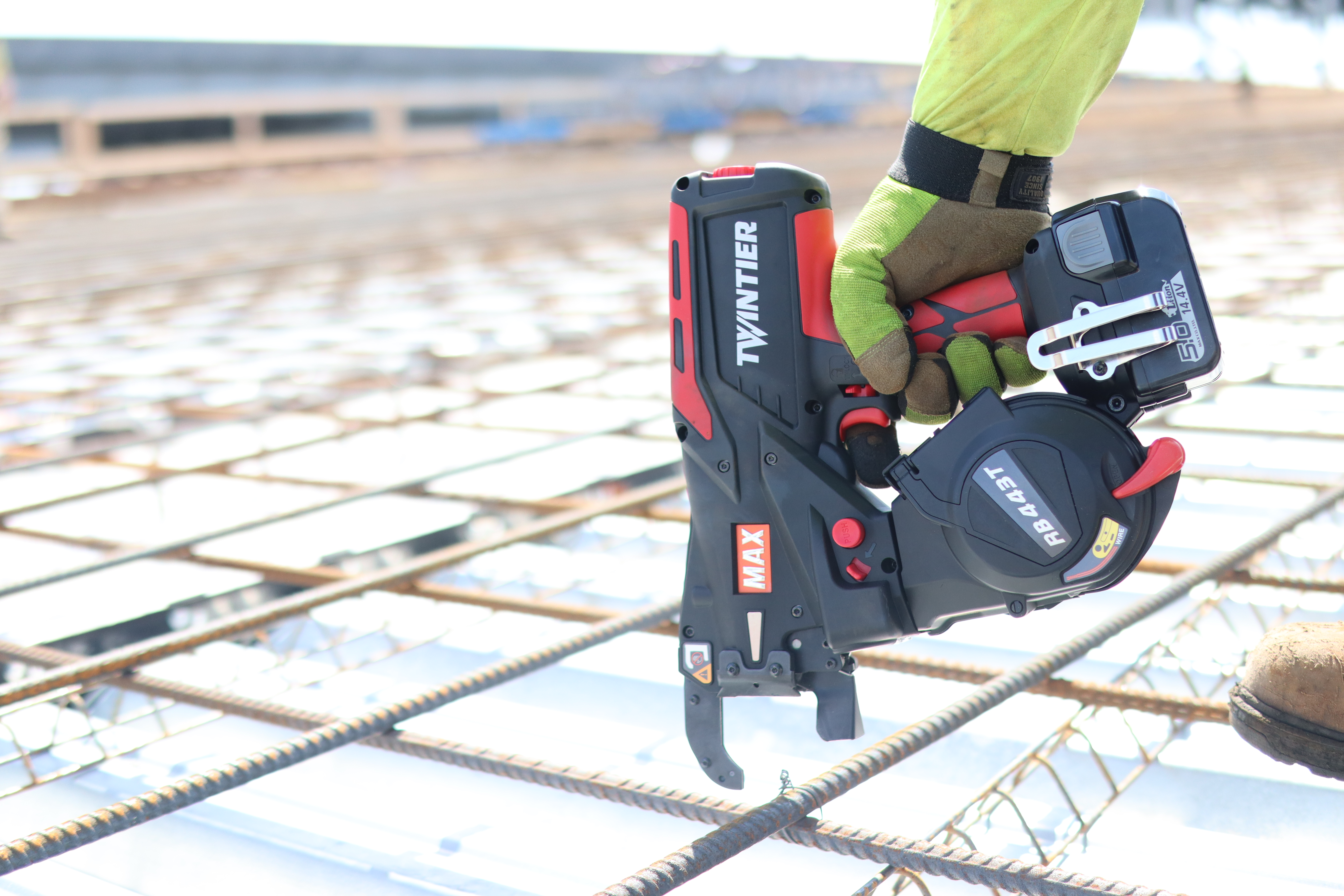 Construction worker using a red MAX nail gun on rebar at a job site