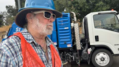 Construction worker in blue hard hat and orange safety vest near street sweeping truck